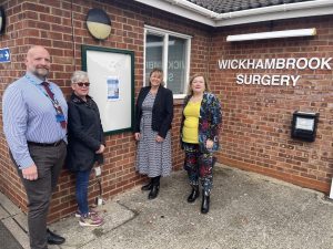 A group of people standing adjacent to a noticeboard fixed to a brick wall.